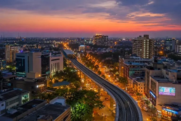 Aerial view of Nagpur news skyline at dusk with elevated metro rail tracks, modern buildings and orange-lit streets, India, realistic cityscape photography, 1200x800px landscape